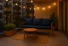 A balcony at dusk with a sofa, coffee table, and string lights. Anteprima dell’immagine prodotto