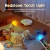 A child is lying on the floor playing with two toy torches, one lit with orange and yellow flames, and the other lit with blue light. A robot vacuum cleaner is in the background. Náhled obrázku produktu