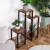 A multi-tiered plant stand with various potted plants and decorative items, placed on a wooden floor next to a sofa. Anteprima dell’immagine prodotto