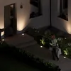 A woman walks up to a house at night, illuminated by ground lights. Produktbild-Vorschau