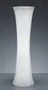 A tall, white, translucent floor lamp with a curved, hourglass shape, standing on a reflective surface against a gradient gray background. Produktbild-Vorschau
