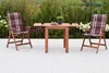 A wooden table and two chairs with cushions are set up on a patio with plants in the background. Produktbild-Vorschau