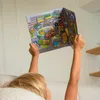 A child is holding up a magnetic play board with a city scene and vehicles. Produktbild-Vorschau