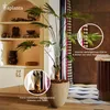 A decorative artificial plant in a pot, placed indoors near a shelf with decorative items and a patterned curtain. Produktbild-Vorschau