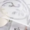 A close-up view of a white sheer curtain with a floral pattern, partially covering a book and a vase. Produktbild-Vorschau
