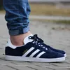 A person wearing blue jeans and navy Adidas Gazelle sneakers. Produktbild-Vorschau