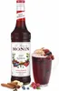A bottle of Monin Spiced Red Berries syrup next to a mug of a red beverage garnished with berries and cream, with cinnamon sticks and ginger in the foreground. Voir les images du produit