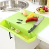 A green cutting board with a pull-out drawer is shown on a kitchen counter next to a sink. Various ingredients like peppers, eggs, garlic, and a knife are on the board. Anteprima dell’immagine prodotto