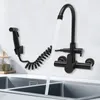 A black kitchen faucet with a spray hose mounted on a wall above a stainless steel sink. Podgląd zdjęcia produktu