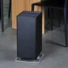 A black air purifier sits on a gray floor next to a wooden table and a black chair. Podgląd zdjęcia produktu