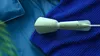 A green handheld garment steamer rests on blue fabric. Produktbild-Vorschau