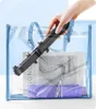 A hand is placing a black selfie stick into a transparent blue tote bag. Inside the bag, there is a book and a folded purple umbrella. Náhled obrázku produktu