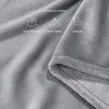 A close-up of a soft, gray fleece blanket with icons and text indicating its versatility for picnics, camping, and home use. Produktbild-Vorschau
