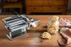 A pasta maker and pasta are displayed on a wooden table. Podgląd zdjęcia produktu