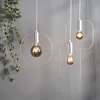 Three modern pendant lights with Edison-style bulbs hang against a gray wall, with a vine of greenery on the left. Podgląd zdjęcia produktu