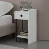 A white bedside table with a drawer and an open shelf, next to a bed. A decorative metal dog figurine is on top of the table. Produktbild-Vorschau