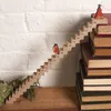 A wooden advent calendar shaped like stairs with numbered steps, featuring a small figurine and a Christmas tree decoration, placed on a shelf next to a stack of books and some greenery. Produktbild-Vorschau