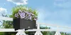 A planter box filled with flowers is mounted on a white railing on a balcony, with a blue sky and trees in the background. Produktbild-Vorschau