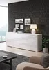 A modern living room with a white sideboard against a dark brick wall, decorated with framed pictures and a lamp. Náhled obrázku produktu