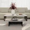 A modern coffee table with a white top and black marble patterned sides, placed in a living room setting with a sofa in the background. Anteprima dell’immagine prodotto