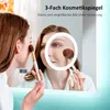 A woman is applying makeup in front of a lighted mirror, with a magnified view of her face shown in the mirror. Produktbild-Vorschau