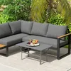 A sectional outdoor sofa and coffee table set on a patio with lush greenery in the background. Náhled obrázku produktu