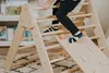 A child's legs are visible as they climb on a wooden play structure indoors. Voir les images du produit