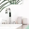 A close-up view of a bathroom sink with a modern chrome faucet, a small decorative cat figurine, and a set of matching soap dispenser and cup. Produktbild-Vorschau