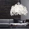 A modern living room with a gray sofa and a dark coffee table, illuminated by a decorative pendant lamp. Produktbild-Vorschau