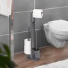A toilet paper holder and brush stand next to a toilet in a bathroom. Náhled obrázku produktu
