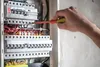 A person's hand is using a screwdriver to work on an electrical panel. Produktbild-Vorschau