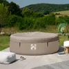 An inflatable hot tub covered with a lid, situated on a patio with a grassy area and hills in the background. Náhled obrázku produktu