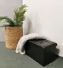 A black storage ottoman with a gray blanket draped over it, next to a potted plant in a woven basket. Podgląd zdjęcia produktu