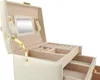 A beige jewelry box with gold accents, opened to reveal its interior compartments and a small mirror. Náhľad obrázku produktu