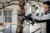 A man is using a cordless chainsaw to trim a tree branch in a garden setting. Podgląd zdjęcia produktu