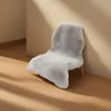 A light gray faux sheepskin rug draped over a chair leg, leaning against a wall with soft lighting. Náhled obrázku produktu