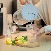 A person pouring water from a pitcher into a glass, with lemons and herbs on a wooden board. Náhled obrázku produktu