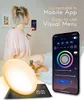 A woman is holding a smartphone, showing an app interface, next to a wake-up light alarm clock. Náhľad obrázku produktu