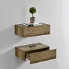Two wooden floating shelves mounted on a light gray wall. The top shelf has books and a small potted plant. The bottom shelf has a pair of sunglasses and an open drawer. Náhled obrázku produktu