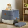 A cat sits on top of a modern, enclosed litter box with a step accessory in front of it. A shelf with a green elephant figurine and a basket is visible in the background. Náhľad obrázku produktu