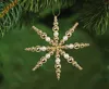 A gold and white snowflake ornament hanging from a Christmas tree branch. Produktbild-Vorschau