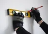 Hands wearing gloves holding a level and a pencil against a white wall. Produktbild-Vorschau