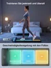 A woman is walking on a treadmill in a bedroom. The image also shows a close-up of the treadmill's control panel with illuminated buttons. Produktbild-Vorschau