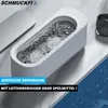 A white ultrasonic cleaner filled with water and small objects is on a marble-like surface next to a watch. Produktbild-Vorschau