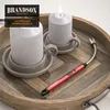 A red electric lighter with a flexible neck is placed on a wooden tray next to two white candles in holders. One candle is lit. Anteprima dell’immagine prodotto