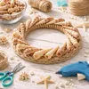 A wreath made of seashells and rope, surrounded by crafting supplies like scissors, twine, and a hot glue gun, on a wooden surface. Produktbild-Vorschau