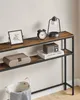 A narrow console table with two shelves is shown against a white wall. The top shelf displays a framed picture, an alarm clock, and a lantern lamp. The lower shelf holds a decorative box and a stack of books with a small radio on top. Produktbild-Vorschau