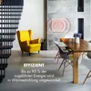 A modern living room with a yellow armchair and a dining table, featuring a wall-mounted infrared heater. Produktbild-Vorschau
