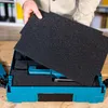 A person is holding black foam inserts over a turquoise tool case. Produktbild-Vorschau