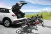 A white car with its trunk open, loaded with a bicycle rack carrying three bicycles, parked near a beach. Anteprima dell’immagine prodotto